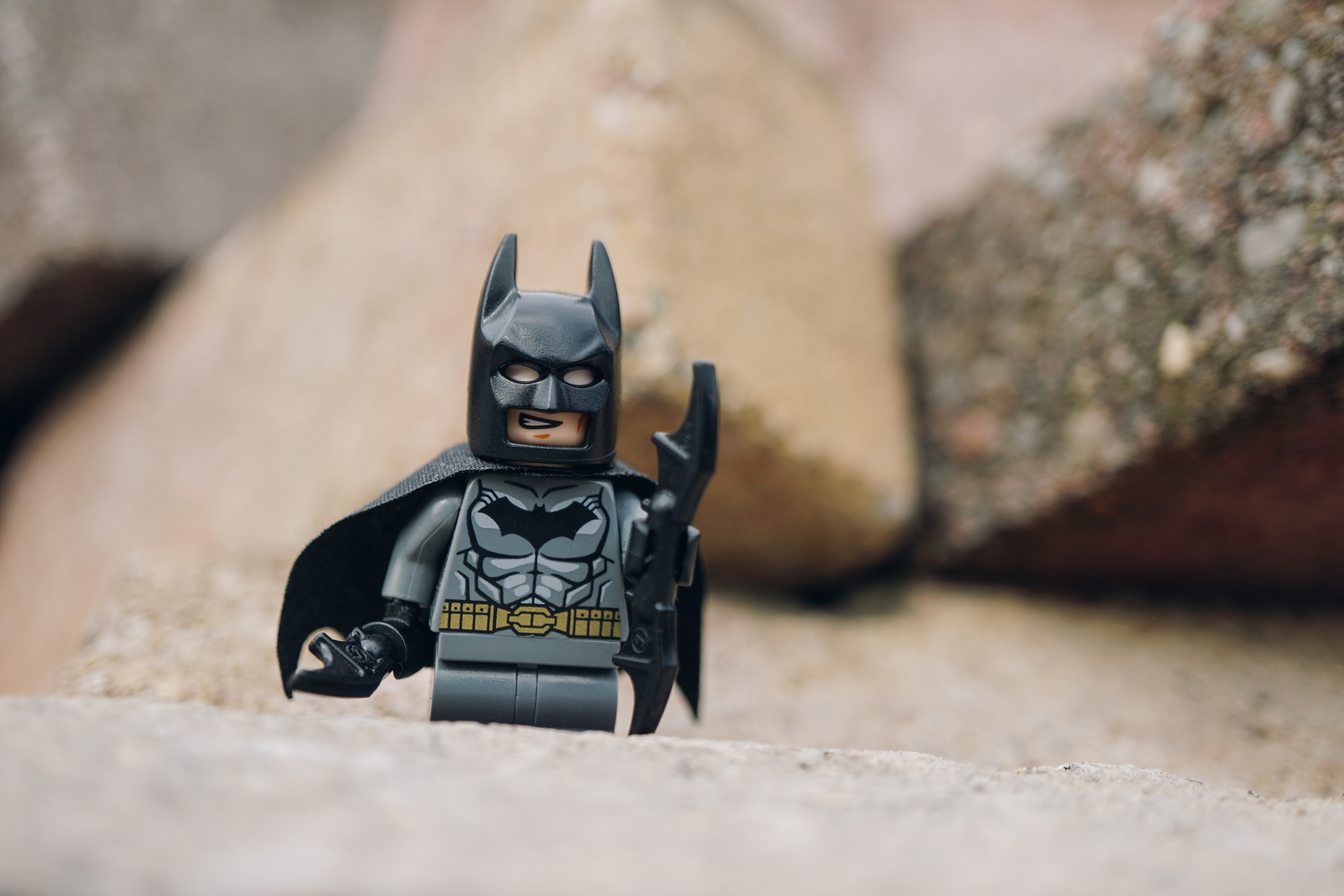 A Lego figure of Batman standing on sandy ground.